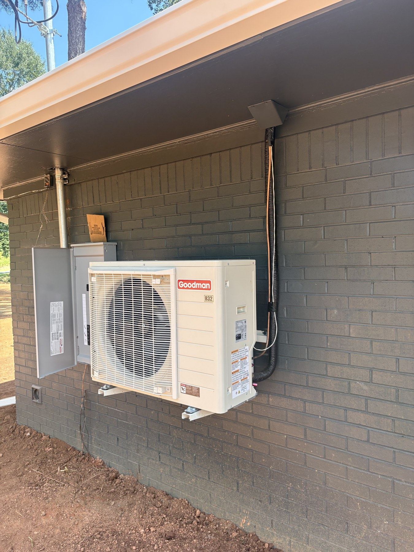 Wall-mounted Goodman outdoor unit installed on a painted brick wall